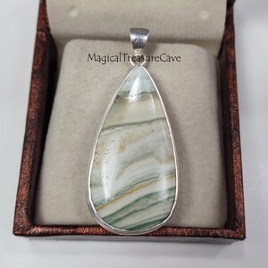 May include: A silver pendant with a teardrop-shaped green and white agate stone. The stone has a layered pattern and is set in a silver bezel.