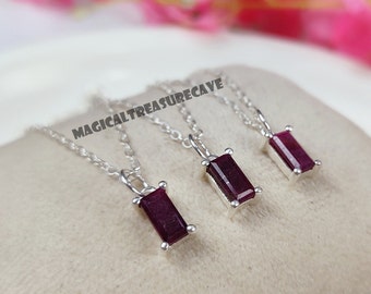 May include: Three silver necklaces with dark red rectangular gemstone pendants. The necklaces are on a white surface.