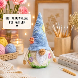 Può includere: Uno gnomo all'uncinetto con un cappello a punta azzurro decorato con un motivo a sole giallo, un corpo color crema con applicazioni floreali colorate, un naso color marrone chiaro e una barba bianca. Modello PDF scaricabile digitalmente.