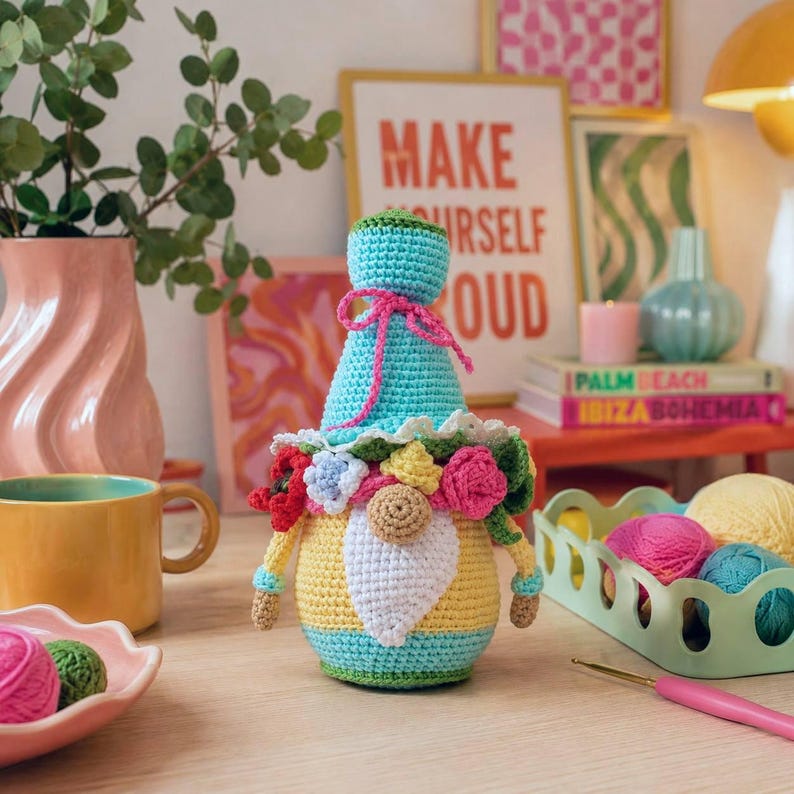 Whimsical crochet garden gnome sitting on a book stack as cozy shelf decor. Colorful dopamine decor amigurumi plush toy, handmade gift idea for flower lovers.