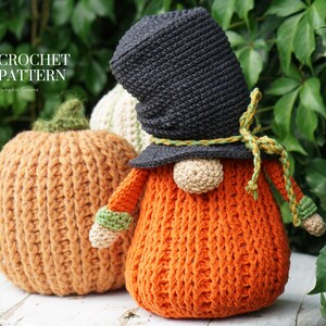 May include: Crochet pattern for a pumpkin gnome. The gnome is orange with a black hat and green accents. The gnome is sitting next to a crocheted pumpkin.