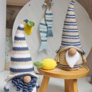 K&ouml;nnte beinhalten: Zwei geh&auml;kelte Gnome mit gestreiften H&uuml;ten und B&auml;rten. Ein Gnom hat eine gelbe Zitrone auf seinem Hut und eine gelbe Zitrone daneben. Die Gnome sitzen auf einem Holzhocker.