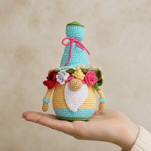 PDF pattern for crocheting a gnome The set may include: a hand-crocheted gnome doll with a blue hat tied with pink yarn, a yellow body and a white beard. The gnome is decorated with multicoloured knitted flowers and green leaves. The doll is approximately 12.7 cm tall.