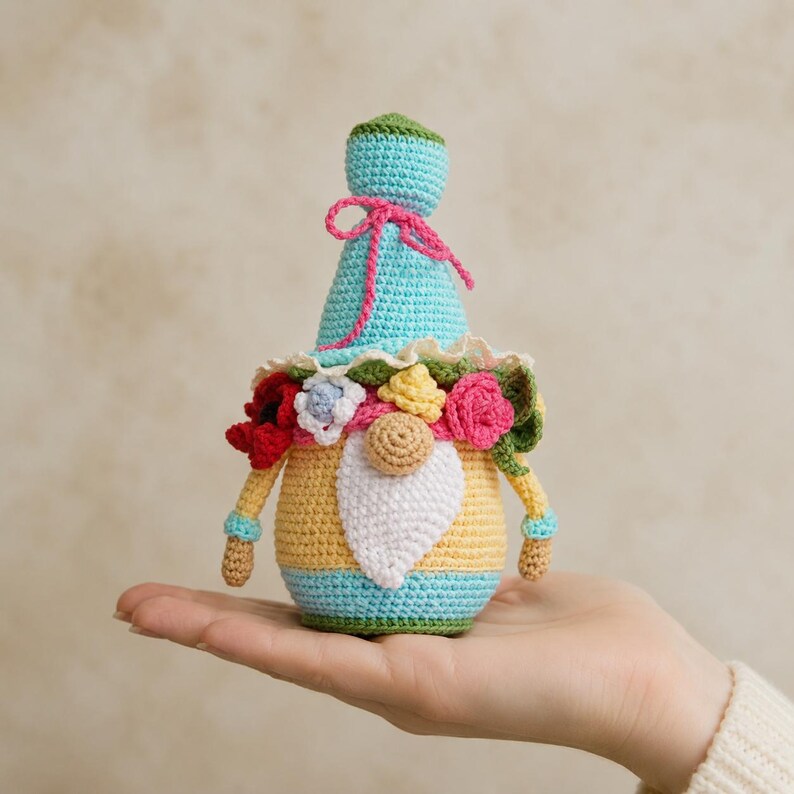 PDF pattern for crocheting a gnome The set may include: a hand-crocheted gnome doll with a blue hat tied with pink yarn, a yellow body and a white beard. The gnome is decorated with multicoloured knitted flowers and green leaves. The doll is approximately 12.7 cm tall.