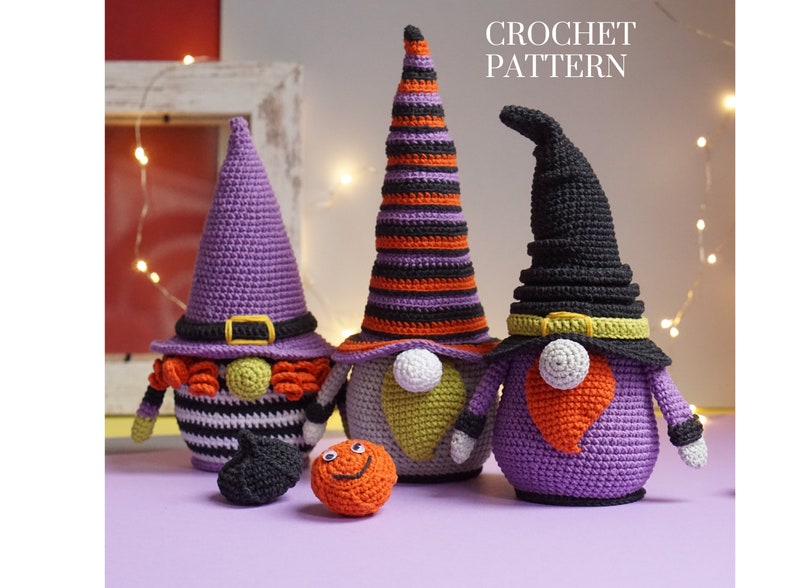 May include: Three crocheted Halloween gnomes with purple, black, and orange striped hats. The gnomes are standing on a purple surface with a small crocheted pumpkin and a black crocheted hat in front of them. The text "CROCHET PATTERN" is at the top of the image.