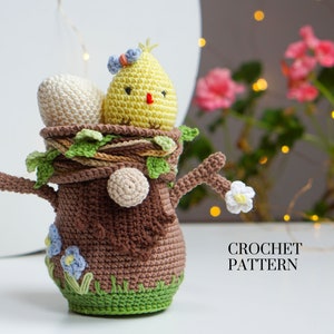 May include: Crochet pattern for a brown tree stump with a yellow chick and white eggs inside. The tree stump has green leaves and blue flowers.