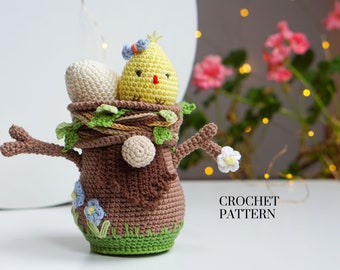 May include: Crochet pattern for a brown tree stump with a yellow chick and white eggs inside. The tree stump has green leaves and blue flowers.