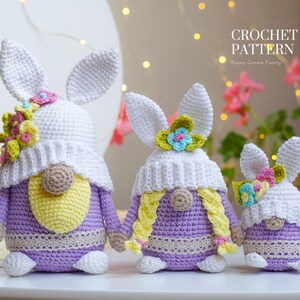 May include: Three crocheted bunny gnome ornaments in different sizes. The largest gnome is purple with a white hat and yellow beard. The middle gnome is purple with a white hat and yellow braids. The smallest gnome is purple with a white hat. All gnomes have floral accents on their hats.