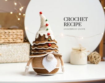 May include: Crochet gingerbread gnome pattern. The gnome is brown and white with a red and green hat. The gnome is sitting on a white surface. CROCHET RECIPE GINGERBREAD GNOME.