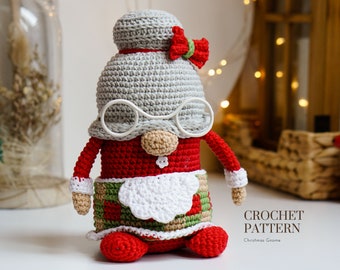 May include: Crochet pattern for a Christmas gnome. The gnome is wearing a red and green outfit with a white beard and a gray hat with a red bow. The gnome is sitting on a white surface.