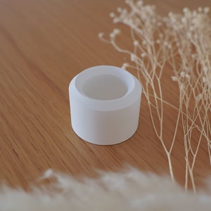 Könnte beinhalten: Ein weißer Keramik-Ringhalter mit einer glatten, abgerundeten Oberfläche. Der Halter ist so konzipiert, dass er einen Ring oder anderen kleinen Schmuck hält.