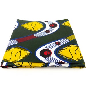 Könnte beinhalten: Ein gefalteter Stoff mit grünem Hintergrund und einem Muster aus gelben Blättern, weißen und blauen geschwungenen Formen und roten Kreisen.