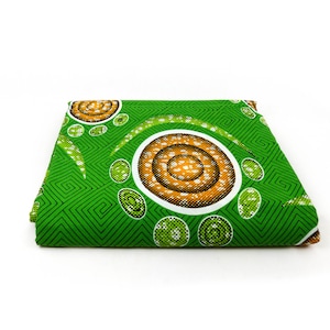 May include: Green fabric with a white and orange geometric pattern. The pattern features circles with concentric rings and a green and white checkered background.