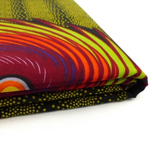 Puede incluir: Una tela doblada con un patrón abstracto colorido. La tela presenta un diseño de remolino en tonos de rojo, naranja, amarillo, verde y azul sobre un fondo negro.