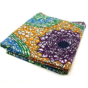 Könnte beinhalten: Ein gefalteter Stoff mit einem farbenfrohen geometrischen Muster. Das Muster zeigt Kreise, Wirbel und Sterne in Blautönen, Grün, Orange, Lila und Weiß.