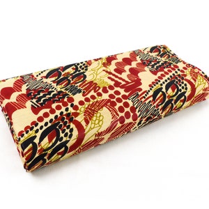 Könnte beinhalten: Ein beigefarbener Stoff mit einem abstrakten Muster in Rot, Schwarz und Gold. Der Stoff ist in der Mitte gefaltet und hat eine glatte Textur.