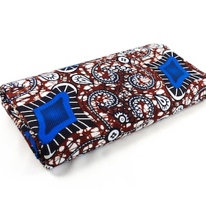 Pode incluir: Um pedaço de tecido dobrado com um padrão paisley marrom, branco e azul. O tecido tem um design geométrico com um losango no centro.