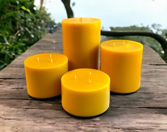 May include: Four yellow pillar candles of varying heights are arranged on a weathered wooden surface. Each candle has multiple wicks visible on top. The candles are cylindrical and have a smooth, solid color.