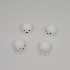 以下が含まれることがあります： 黒い笑顔の顔をした、小さな白いお化けの形をした4つの置物。 各お化けにはフリルのベースがあり、白い表面に配置されています。 これらは、ハロウィーンまたは不気味をテーマにした装飾である可能性があります。