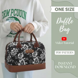 Könnte beinhalten: Eine schwarze Duffle-Bag mit weißem Blumenmuster und braunen Lederakzenten. Die Tasche hat braune Griffe und einen braunen Boden. Der Text "Duffle Bag" und "One Size" sind sichtbar.
