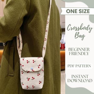 May include: A cream-coloured corduroy crossbody bag featuring a repeating red cherry pattern, a long adjustable strap, and a single light blue snap button closure. The text on the image reads ONE SIZE, Crossbody Bag, BEGINNER FRIENDLY, PDF PATTERN, INSTANT DOWNLOAD.