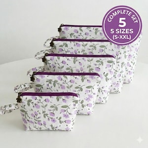 May include: A set of five floral print cosmetic bags in varying sizes, from small to extra-extra large. The bags feature a white background with a pattern of purple flowers and green leaves. Each bag has a dark purple zip and trim, and a small handle.