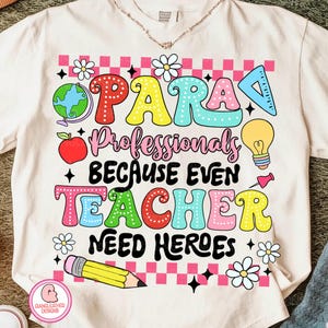 May include: Cream-colored t-shirt with a colorful graphic design. The design includes the words "PARA Professionals BECAUSE EVEN TEACHERS NEED HEROES" in various bright colors, along with illustrations of a globe, apple, pencil, and flowers.