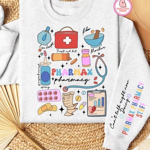 May include: A light grey sweatshirt with a colourful graphic design featuring various pharmacy-related items, including a first aid kit, mortar and pestle, pills, bandages, a stethoscope, and the text "PHARMAX pharmacy". The right sleeve has the text "Can't talk right now Doing PHARMAX PHARMACY STUFF".