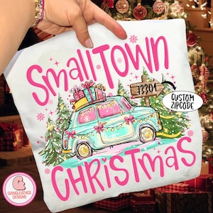 May include: White pillow with the words "Small Town Christmas" in pink script. A teal car with Christmas lights and presents on top is featured. A sign with a zip code and the words "Custom Zipcode" are also visible.
