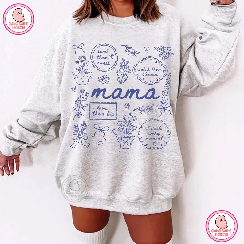 May include: Light gray sweatshirt with blue floral and text design. The word "mama" is in the center, surrounded by floral illustrations and phrases like "spoil them sweet" and "cherish every moment".