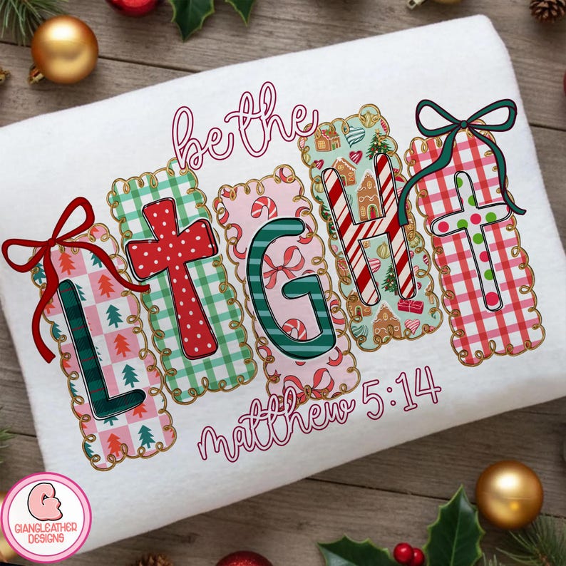 May include: White Christmas towel featuring the phrase "be the LIGHT" in festive lettering. The design incorporates crosses, candy canes, and gingerbread houses. The text "Matthew 5:14" is also included.