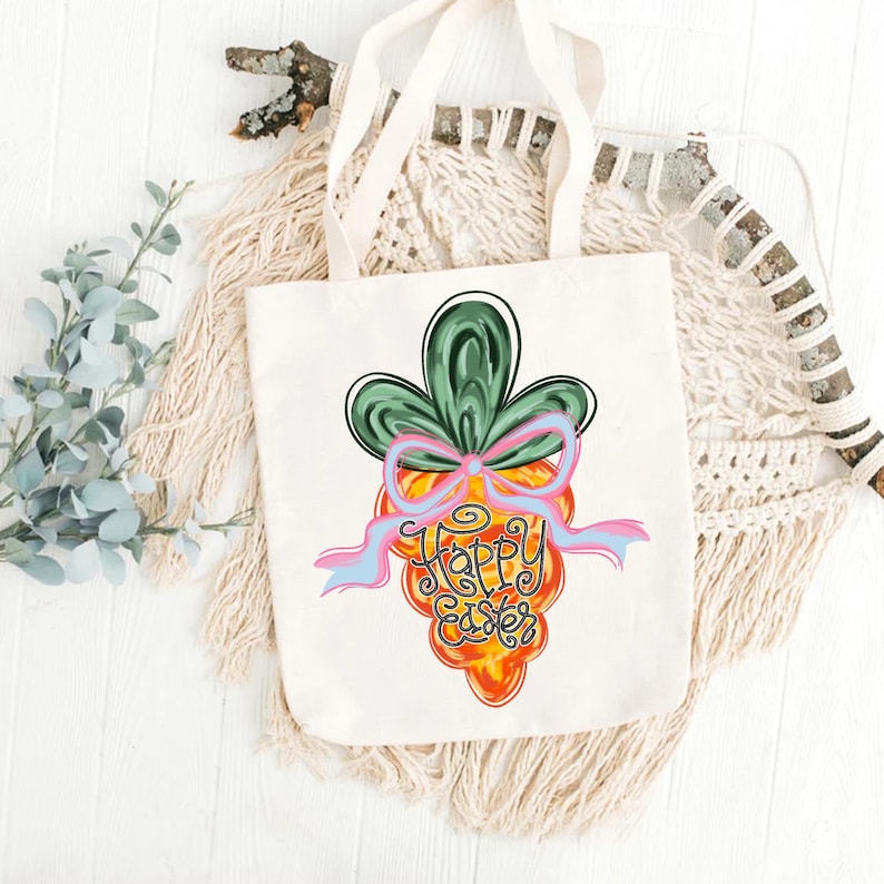 May include: A white tote bag with a colorful cartoon carrot design. The carrot has a green top, a pink bow, and the words "Happy Easter" written on it.