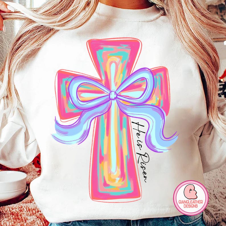 May include: A white sweatshirt with a colorful cross design and the text "He is Risen" printed on the front.