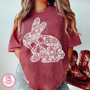 Może przedstawiać: Bordowy t-shirt z białym haftem w kształcie królika. Królik ma kokardkę na szyi.