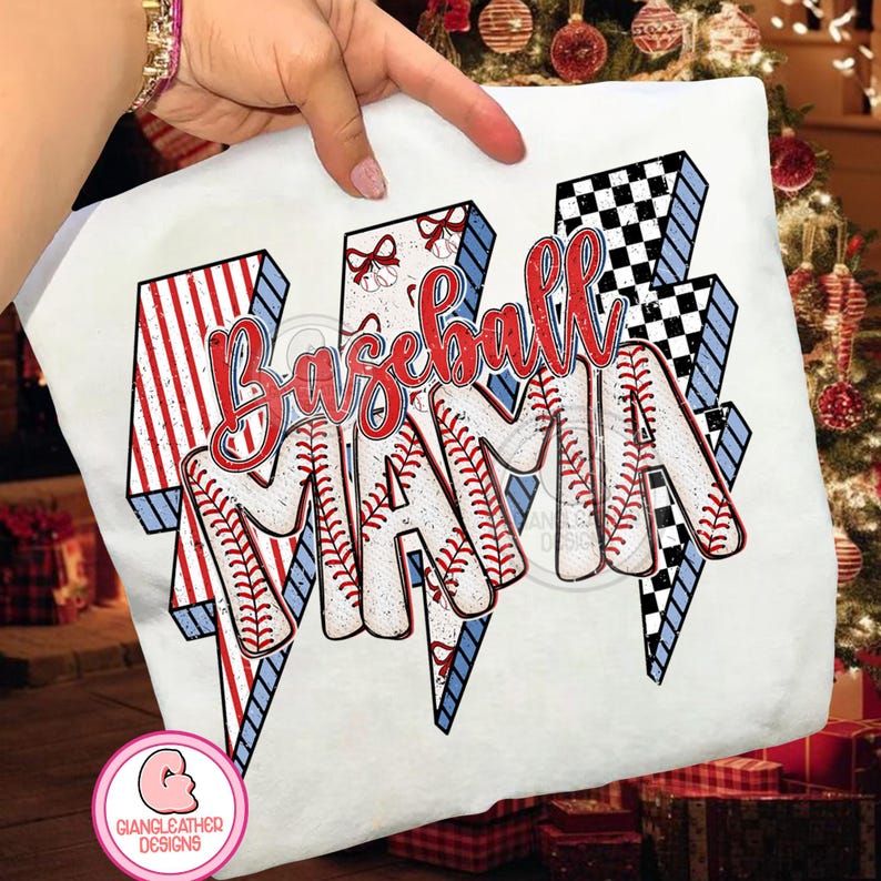 May include: White t-shirt with a baseball-themed design. The design features the words "Baseball Mama" in red script, with the letters styled as baseballs. The background includes red and white striped lightning bolts and a black and white checkered lightning bolt.