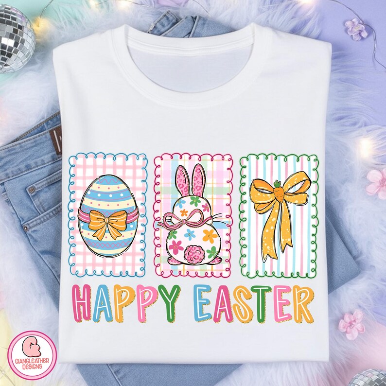 May include: White t-shirt with a colorful Easter design. The design includes an Easter egg, a bunny, and a bow, each within a decorative frame. The words "HAPPY EASTER" are printed in colorful letters below the images.