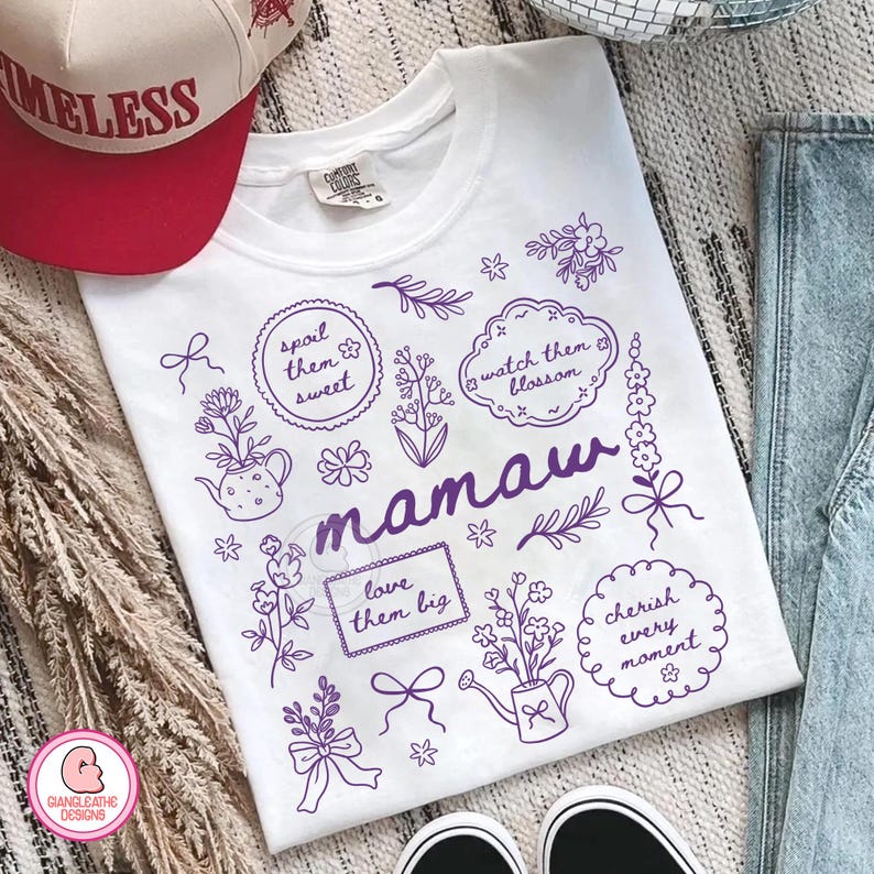 May include: White t-shirt with purple floral illustrations and the word "mamaw". The design includes phrases like "spoil them sweet" and "cherish every moment". A red and white baseball cap is visible.