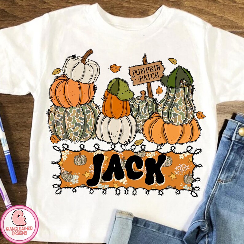 May include: White t-shirt featuring a colorful pumpkin patch design. The design includes stacked pumpkins in orange, white, and camouflage patterns, with a sign that reads "Pumpkin Patch" and the name "Jack".