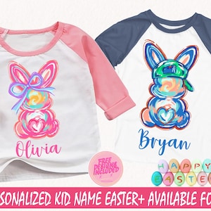 Puede incluir: Dos camisetas de Pascua personalizadas con ilustraciones de conejos coloridos. La camiseta rosa dice "Olivia" y la camiseta azul dice "Bryan". Las camisetas son blancas con un diseño de manga raglan rosa y azul. Las camisetas están rodeadas de huevos de Pascua coloridos que dicen "Feliz Pascua".