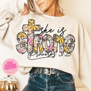May include: A white sweatshirt with a floral design that says "She is Strong Proverbs 31:25".