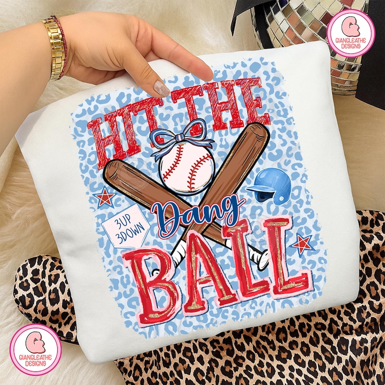 May include: White baseball-themed sweatshirt with a blue leopard print background. The design features a baseball, crossed bats, and the text "HIT THE BALL, Dang". Includes a blue baseball helmet and stars.