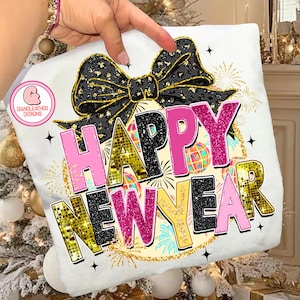 May include: White t-shirt with a Happy New Year design. The design features a black bow with gold accents, the words "Happy New Year" in pink, black, and gold, and fireworks.