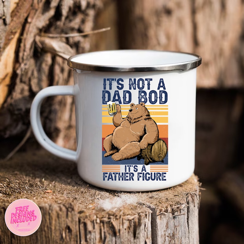 May include: White enamel camping mug with a brown bear holding a beer and sitting on a barrel. The mug has the text "It's not a dad bod, it's a father figure" in black.