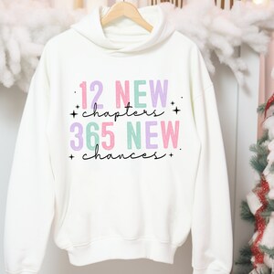 May include: White hoodie with a pink, purple, and green graphic print that says "12 NEW chapters + 365 NEW chances +"