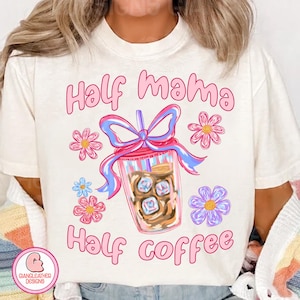 May include: White t-shirt with pink text that reads "Half mama Half coffee". The text is surrounded by a pink bow, a blue ribbon, and pink and purple flowers.