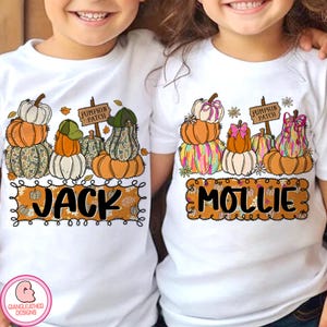 Puede incluir: Dos camisetas blancas con diseños de calabazas. Una camiseta dice "Jack" y la otra "Mollie" en una fuente decorativa. Cada camiseta presenta calabazas apiladas en varios colores y patrones, con un letrero de "Pumpkin Patch".