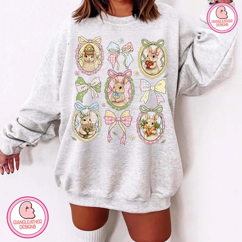 K&ouml;nnte beinhalten: Ein hellgraues Sweatshirt mit einem sich wiederholenden Muster von Osterhasen in verzierten Rahmen, durchsetzt mit bunten Schleifen. Die Hasen halten Ostereier, Blumen und Karotten. Das Design ist in Pastellfarben gehalten und erzeugt einen skurrilen und festlichen Look.