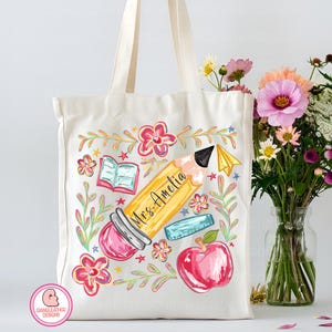 May include: Cream-colored tote bag featuring a colorful school-themed design. A large yellow pencil with "Mrs. Amelia" written on it is the focal point, surrounded by flowers, an apple, an eraser, and an open book. The bag has cream-colored handles.