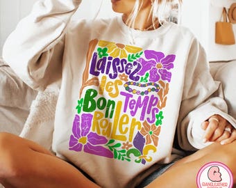 May include: Cream-colored sweatshirt with a colorful floral design and the phrase "Laissez les Bon Temps Rouler" in purple, green, and yellow. The design includes a beaded necklace and various flower illustrations.