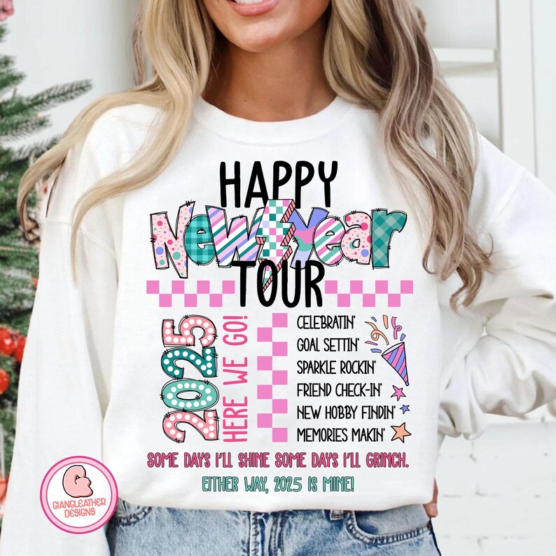 May include: White sweatshirt with a colorful graphic design that says "Happy New Year Tour 2025" with a pink and white checkered background. The graphic also includes the text "Here We Go!" and a list of activities for the new year, including "Celebratin, Goal Settin, Sparkle Rockin, Friend Check-In, New Hobby Findin, Memories Makin". The graphic ends with the text "Some days I'll shine some days I'll Grinch. Either way, 2025 is mine!"